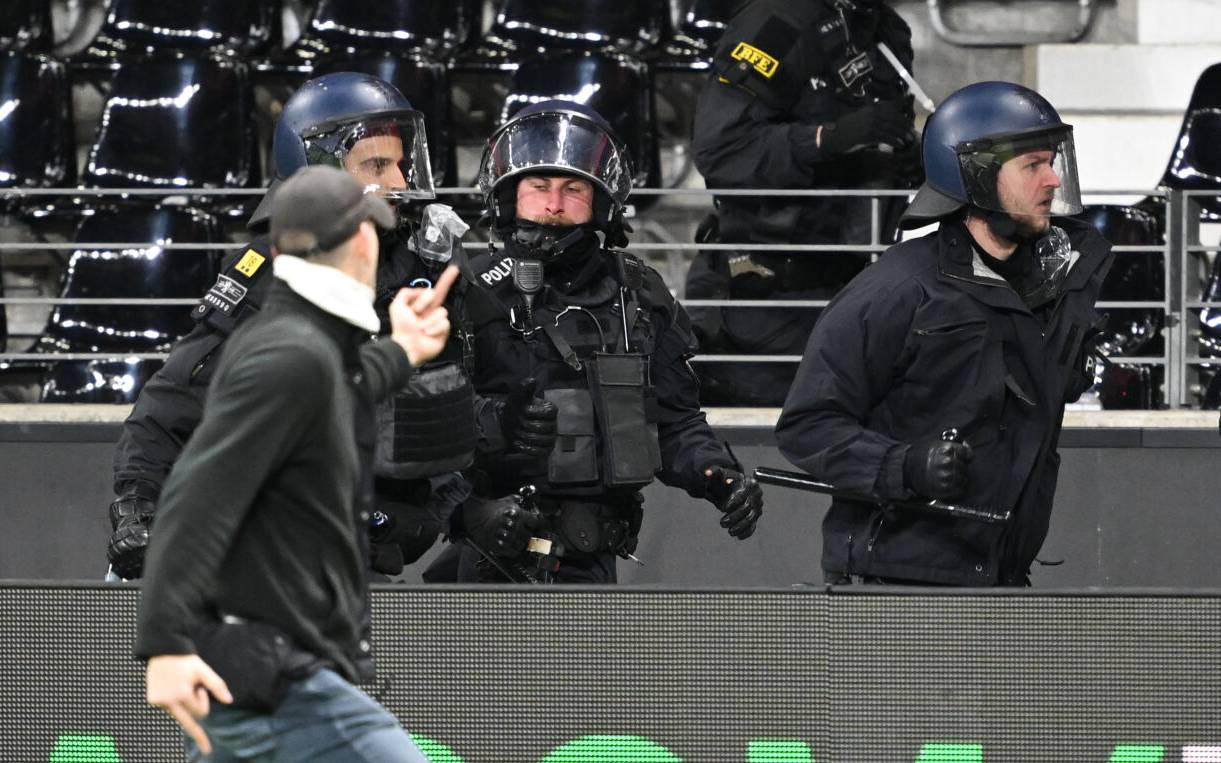 Ein Fußballfan zeigt Polizisten den Mittelfinger, als er an ihnen vorbeiläuft.