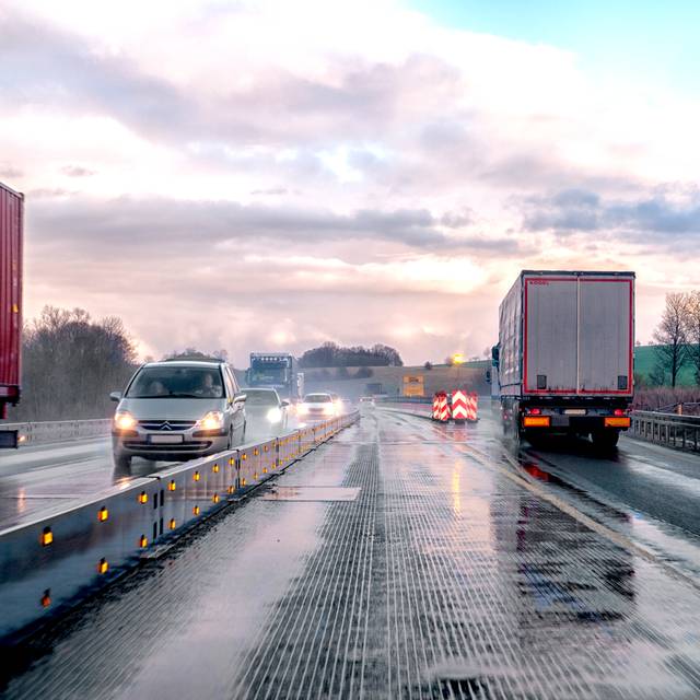 Eine verengte Fahrspur auf einer deutschen Autobahn, die ein nass-kaltes Wetter zeigt, bei dem im Gegenverkehr die Scheinwerfer der Autos erkennbar sind.
