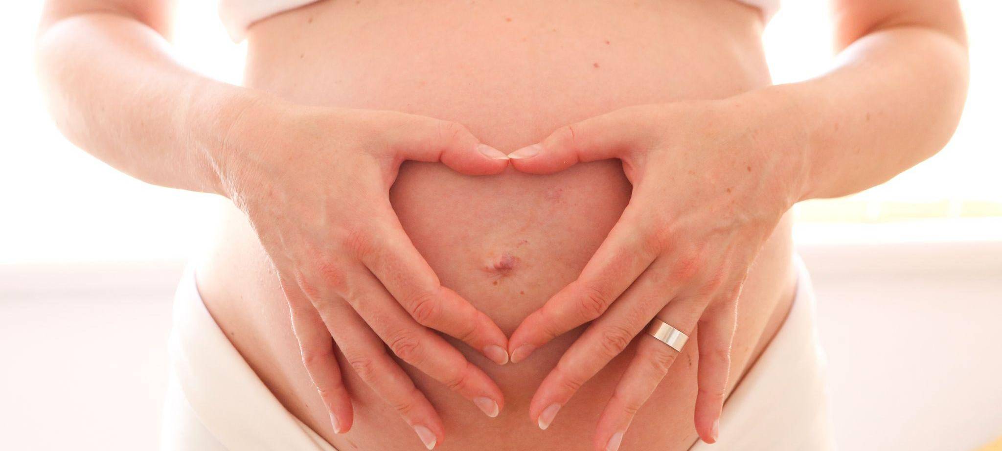 Eine schwangere Frau hält zum Herz geformten Hände vor den Bauch