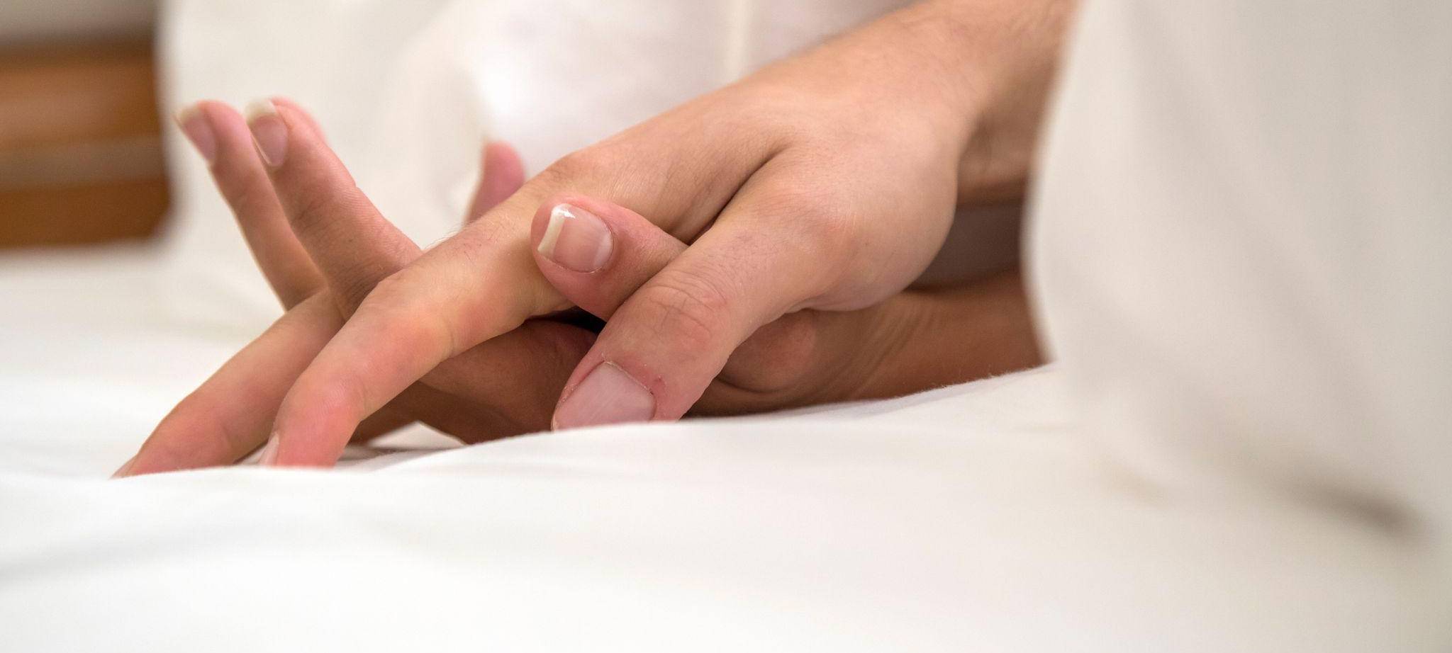 Zwei ineinander liegende Hände sind unter einer Decke zu sehen